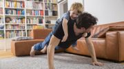 Father doing push ups in living room with son on his back Father doing push ups in living room with son on his back