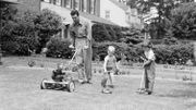 Father cutting lawn with power mower, two boys using toy rake and mower. Father cutting lawn with power mower, two boys using toy rake and mower.