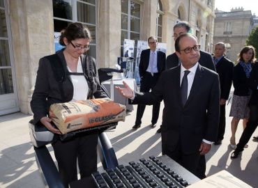 Une jeune femme montre au président Hollande comment elle soulève sans effort un sac de ciment grâce à un exosquelette d’assistance. Une jeune femme montre au président Hollande comment elle soulève sans effort un sac de ciment grâce à un exosquelette d’assistance.