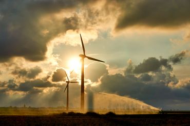 Two wind turbines and irrigating crop water gun or water spray at sunset Two wind turbines and irrigating crop water gun or water spray at sunset