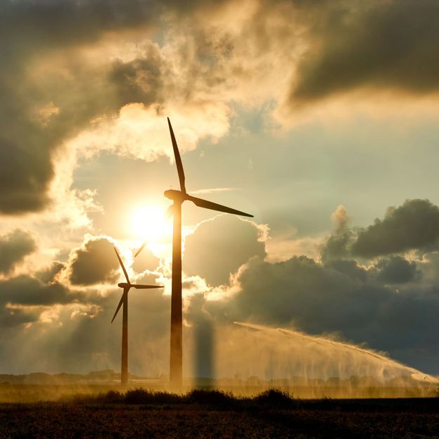 Two wind turbines and irrigating crop water gun or water spray at sunset Two wind turbines and irrigating crop water gun or water spray at sunset